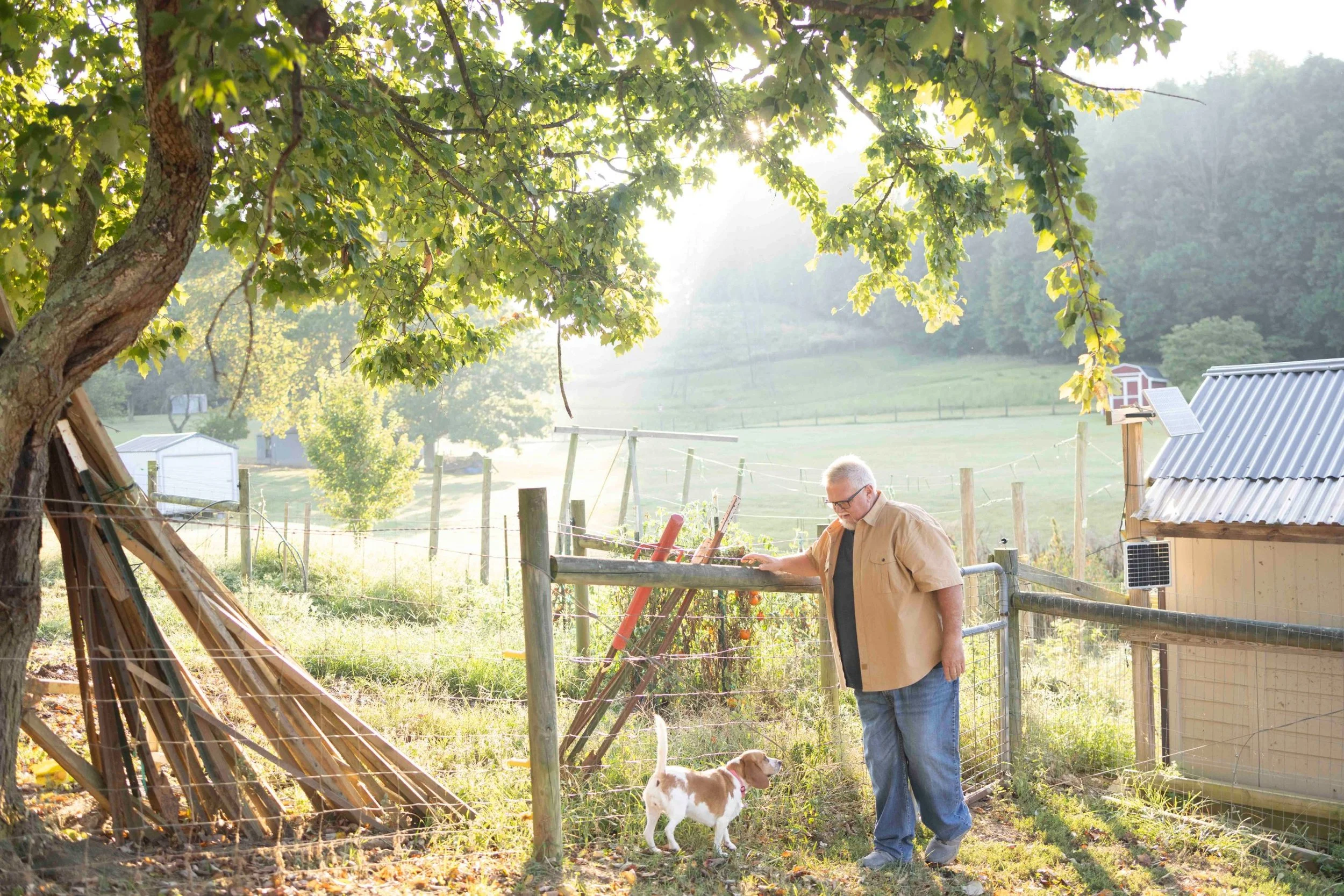 Patient story photography: man petting a beagle at a garden fence in soft morning light