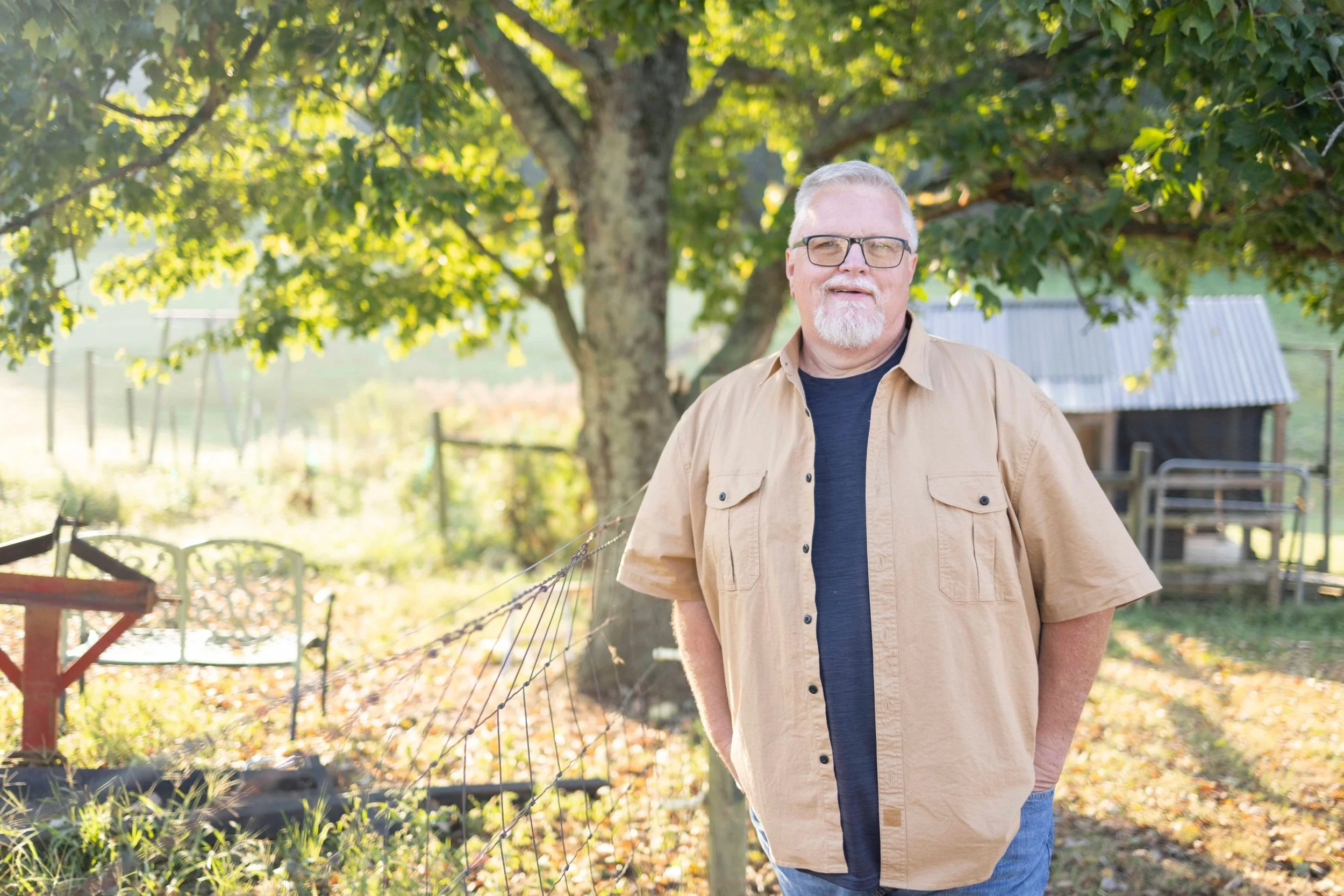 Healthcare brand portrait: smiling man in glasses standing under a tree on a farm in autumn light
