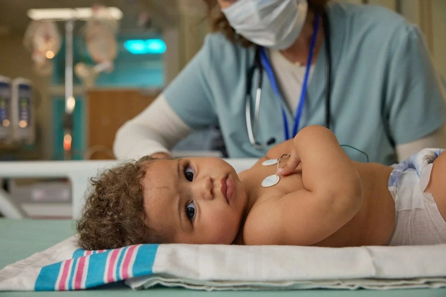Masked nurse examining an infant on a hospital changing table, Beyfortus infant healthcare photography