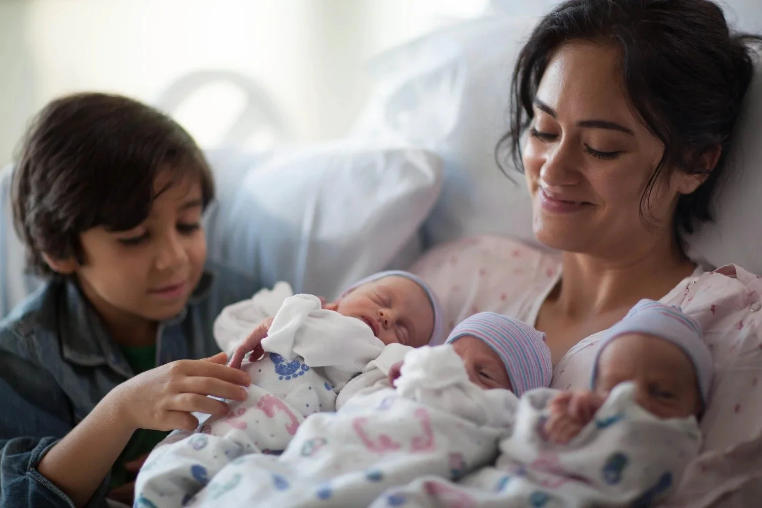 Mother and young son with newborn twins in a hospital bed, family healthcare photography