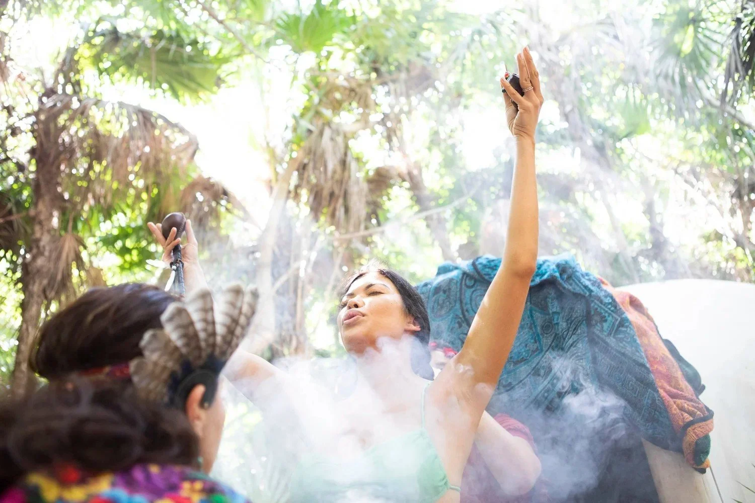 Women in a smoke ceremony with feathers and a raised hand under sunlight, women's retreat ceremony photography in Riviera Maya, Mexico