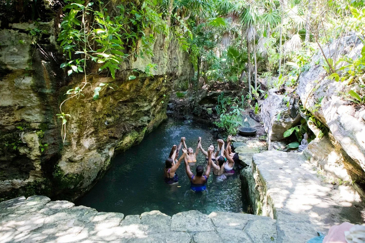 Group of women gathered in a natural rock pool surrounded by greenery, women's retreat photography in Riviera Maya, Mexico