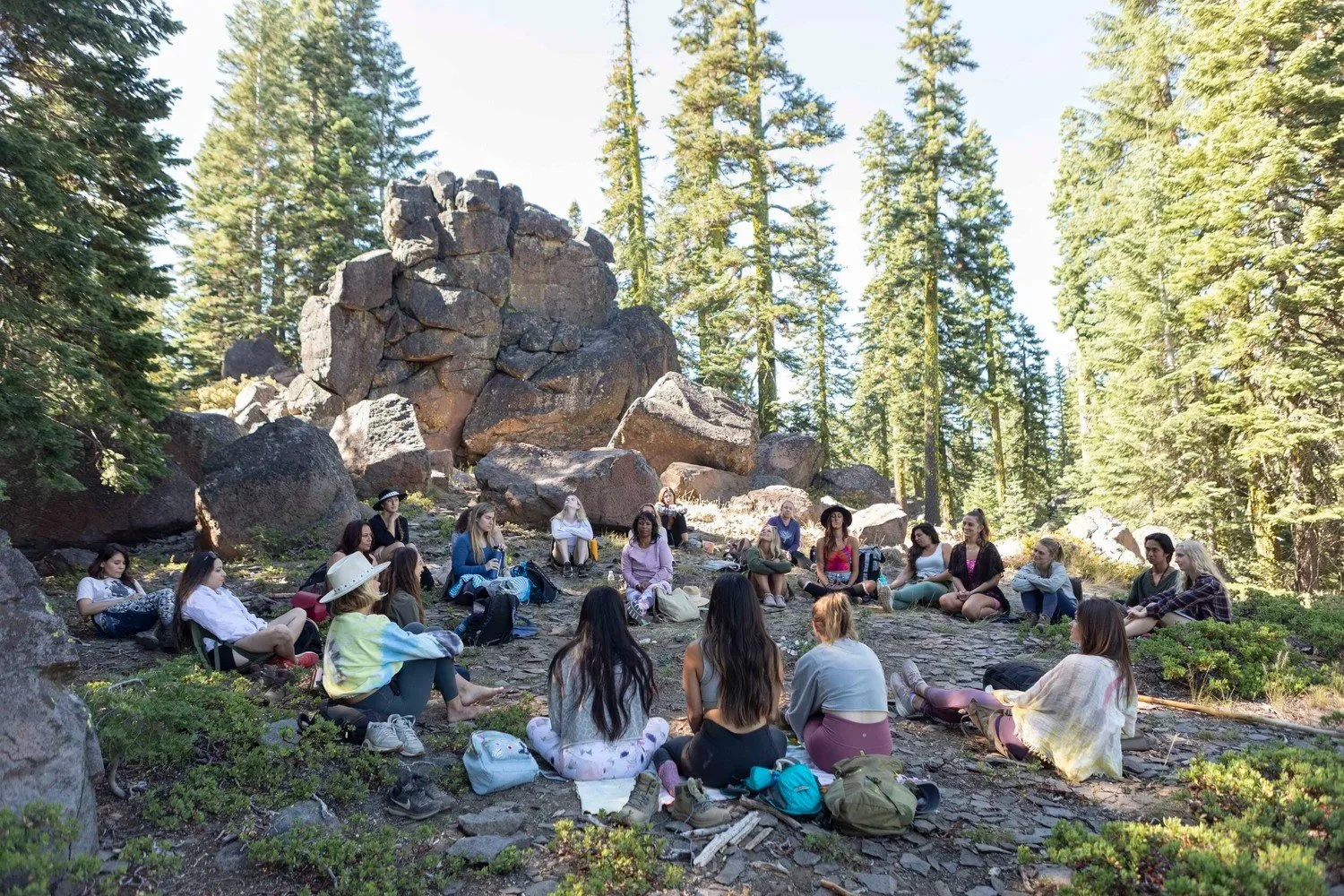 Group seated in a circle on rocks among pine trees, Mount Shasta women's retreat workshop photography