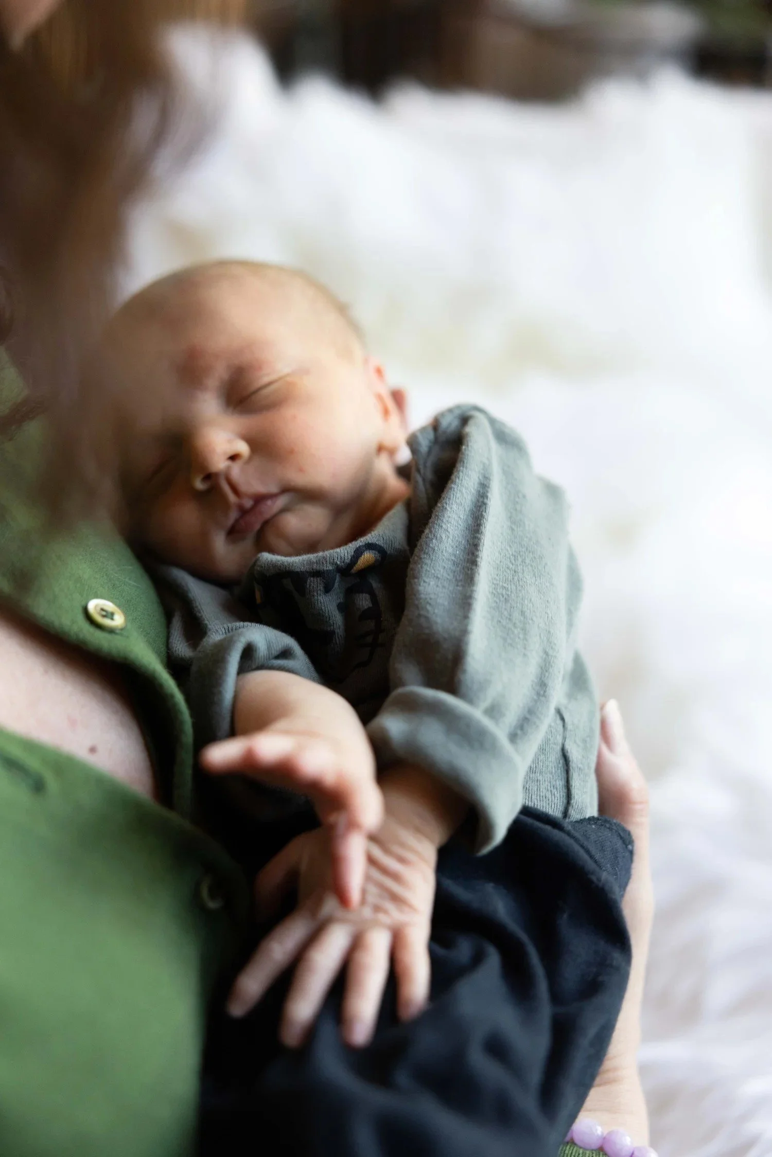 Newborn in a green outfit held in a parent's arms, pediatric and family healthcare photography