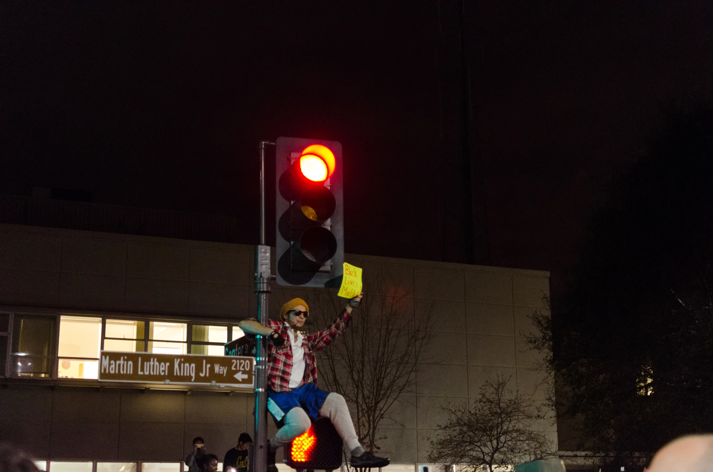 Man sits on signal post in front of Berkeley Police Station - photo by Kyle Cameron