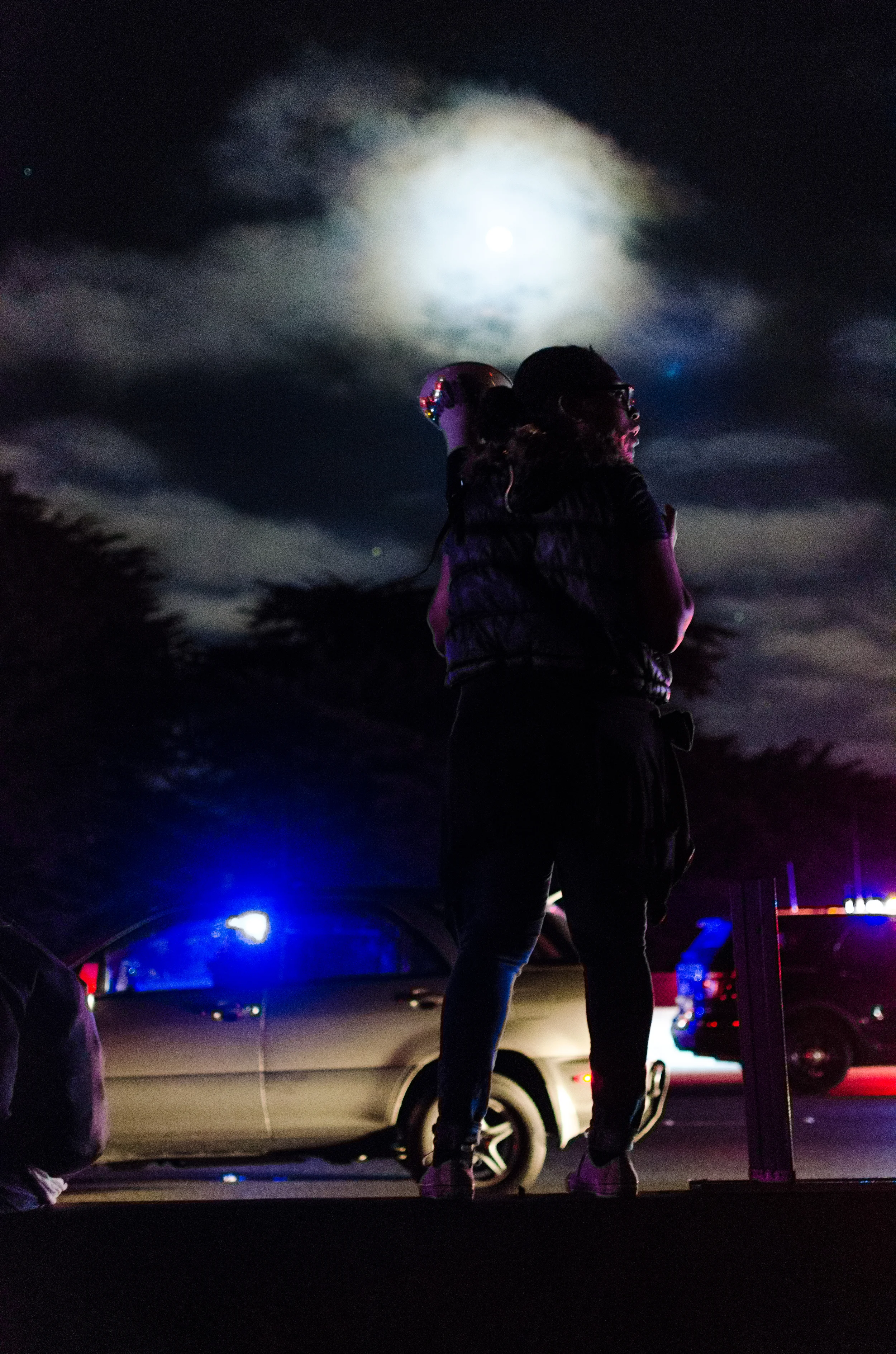Woman with megaphone set against the moon giving instructions to protesters advancing Southward on Interstate 80 - photo by Kyle Cameron
