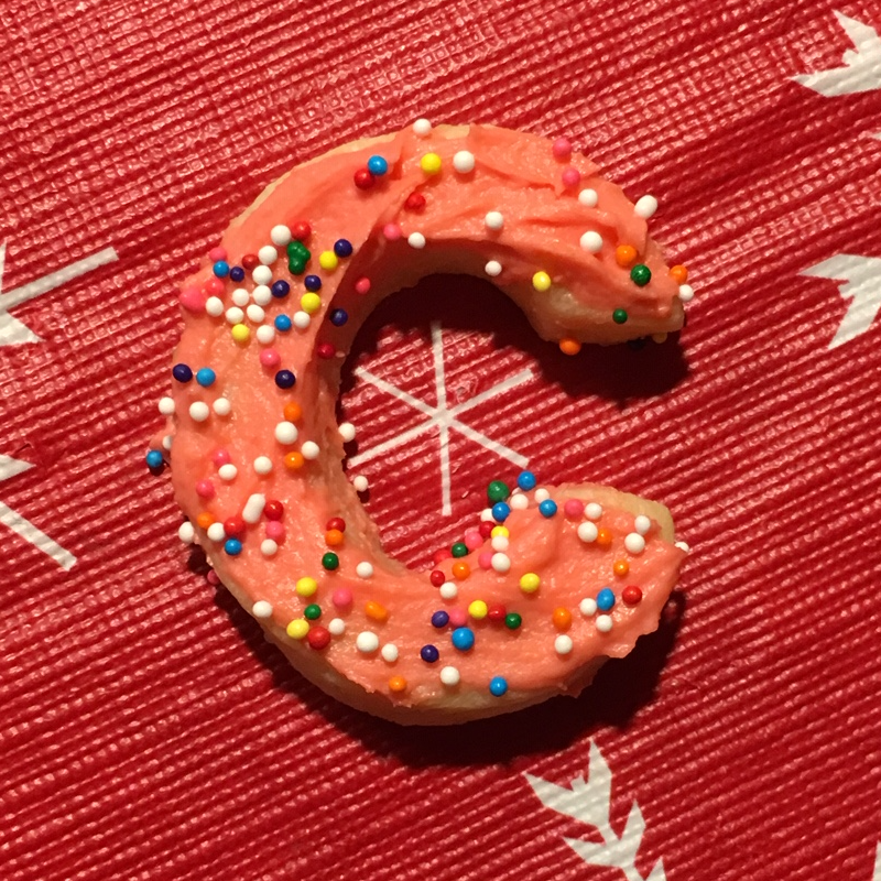 Sugar cookie with pink frosting and rainbow sprinkles on holiday tablecloth, mixed media, 2018