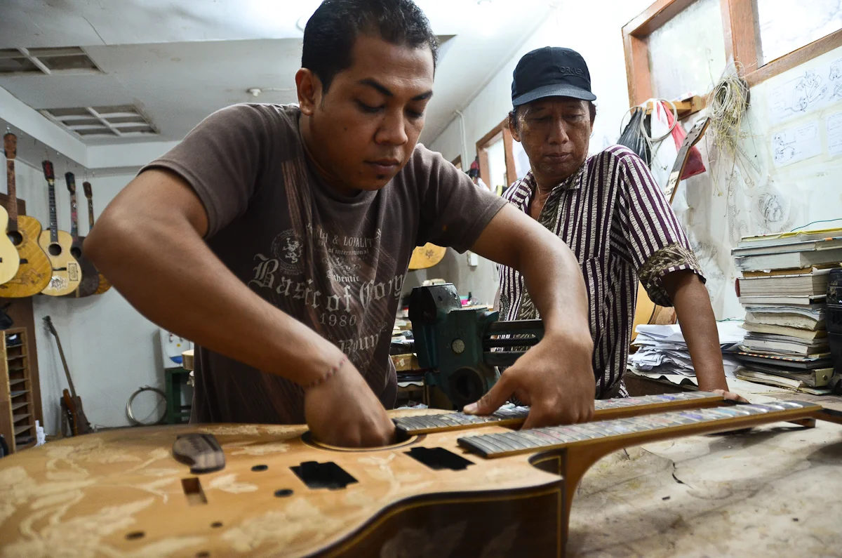 Wayan Tuges looks on as an assistant assembles a new model: a double-necked acoustic/electric hybrid guitar.