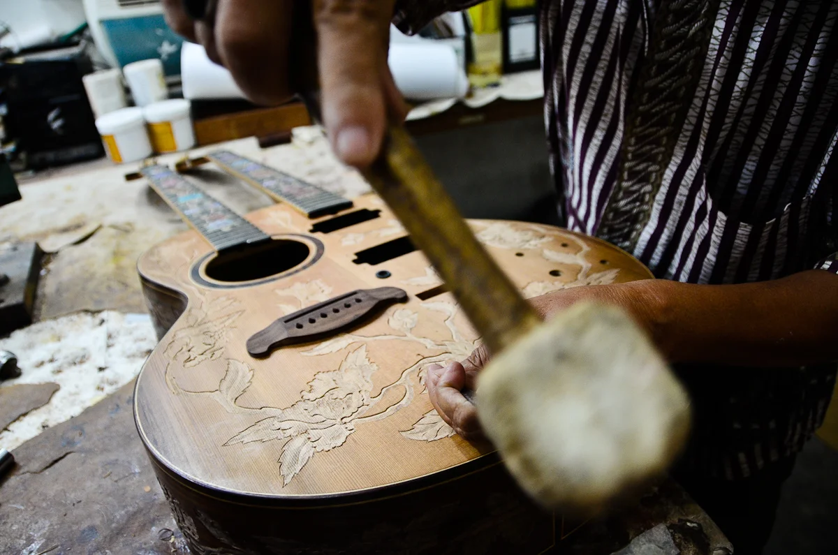 Wayan Tuges uses a mallet and chisel to etch a pattern into the face of a new guitar.