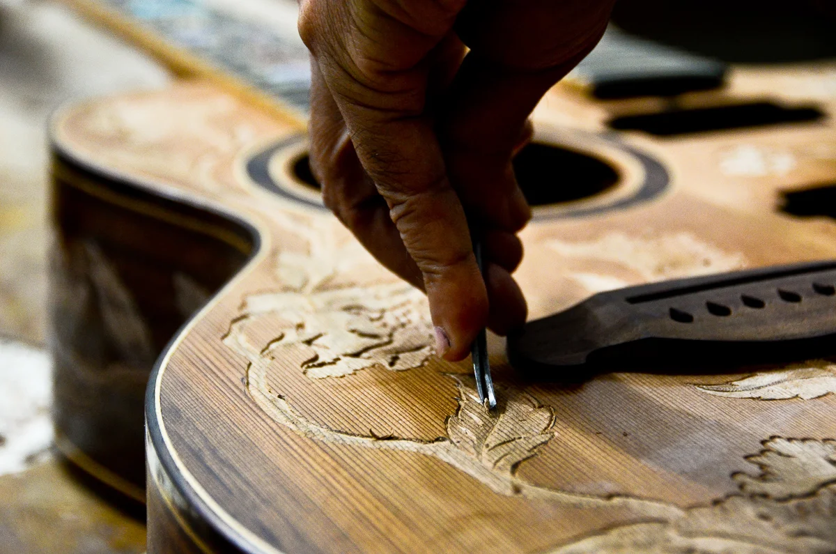 Wayan Tuges uses a chisel to etch a pattern into the face of a new guitar.