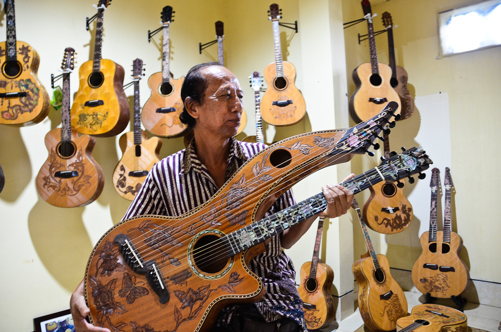  Wayan Tuges holds up a double-necked guitar in his workshop storage room. 