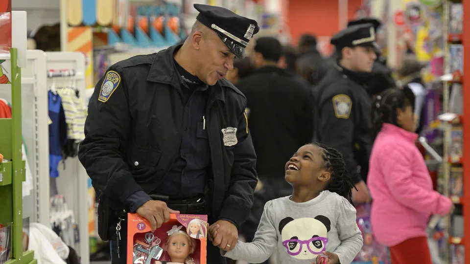 SANTAS IN BLUE: Officer Jorge Dias helps Janiyah Woodley, 7, carry her new doll at the Dorchester target yesterday. (photo by Chris Evans)