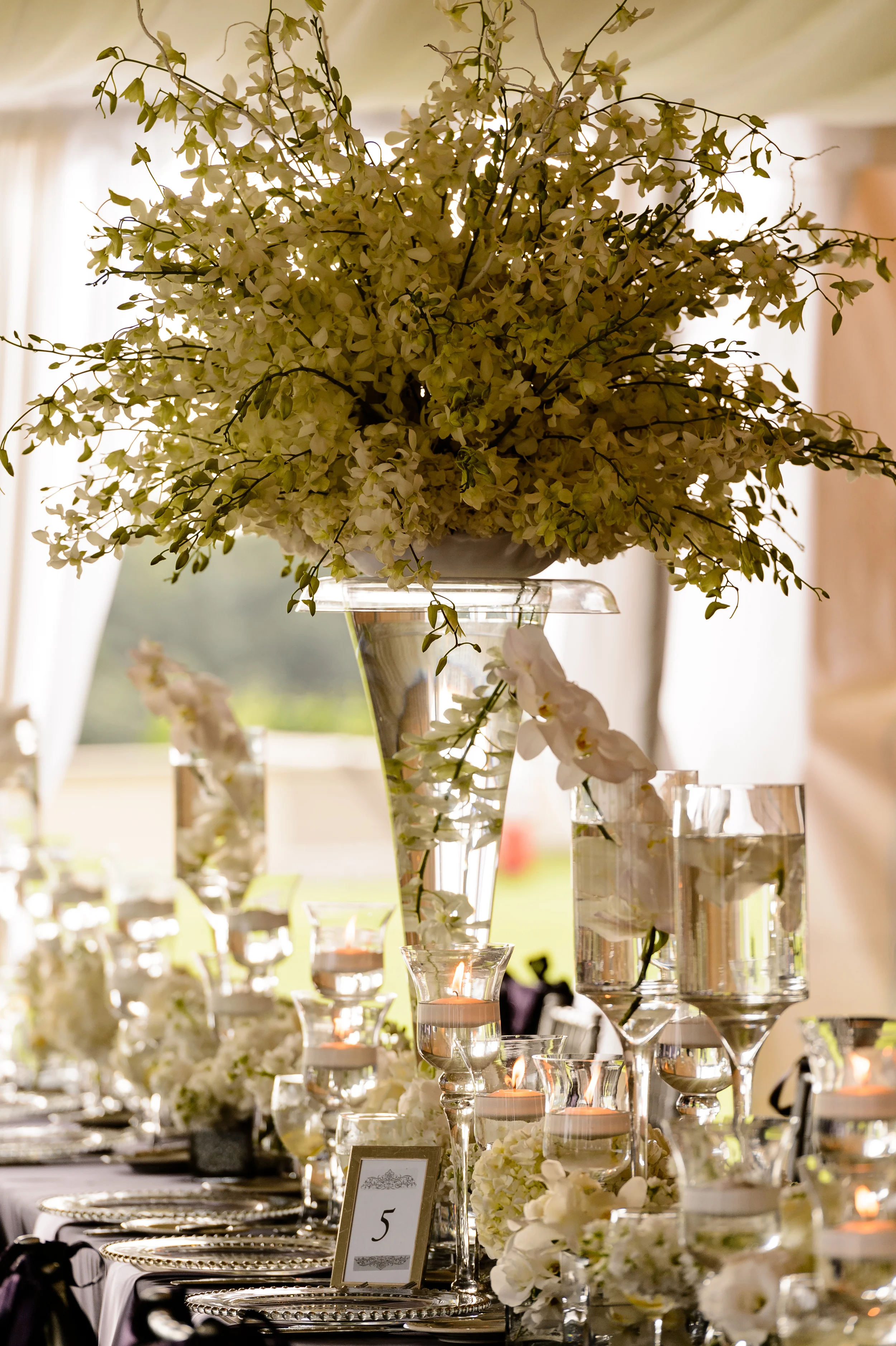Grand Centerpieces of white orchids, multiple heights of candles, goblets with floating candles, white grouping of flowers, all different and giving texture to the feasting tables.