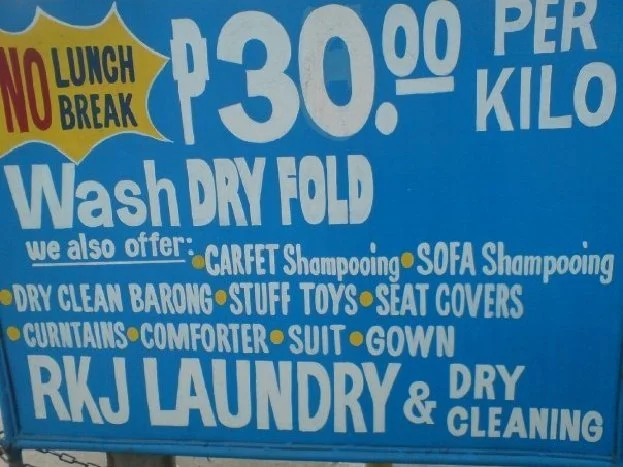 Sign says: No lunch break. P30.00 per kilo. Wash. Dry. Fold. We also offer: Carfet Shampooing. Sofa Shampooing. Dry clean barong. Stuff toys. Seat covers. Curntains. Comforter. Suit. Gown. RKJ Laundry & Dry Cleaning"