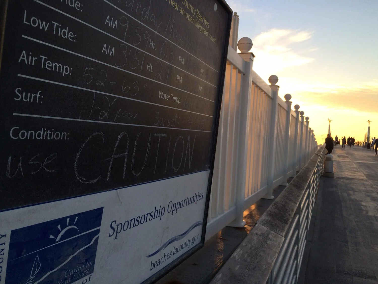 A sign at the Hermosa Pier in Southern California warns of high tides and rough conditions. The pier, and others throughout the South Bay of Los Angeles, is popular among Filipinos for fishing. The area is projected to be hit by sea-level rise in the coming decades. (Photo by Dorian Merina).