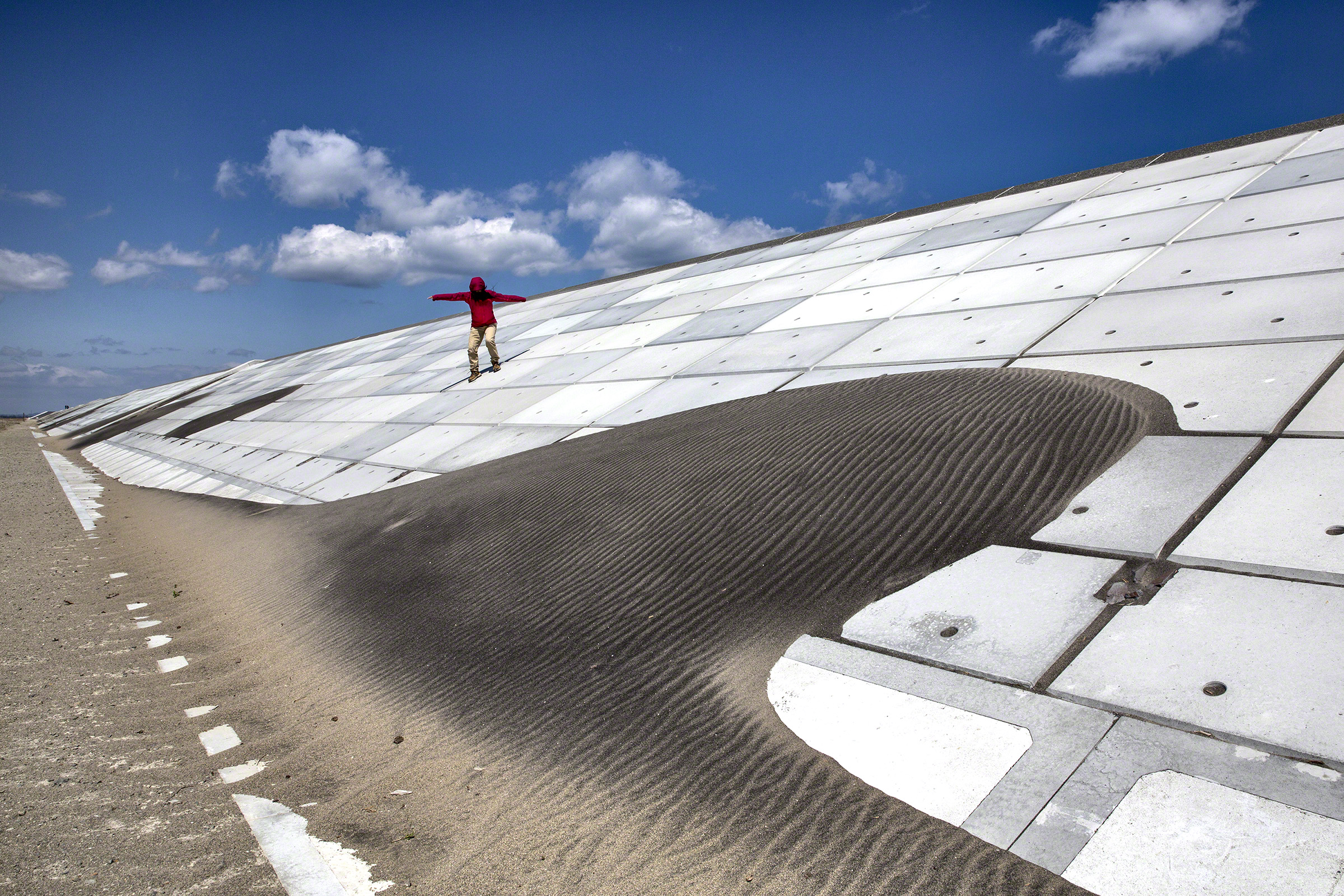 A woman makes her way down the seawall along the Kitakama and Ainokama coastline inSendai, Japan. After the tsunami in 2011, the Japanese government has spent billions of yen on the reconstruction of a 31.8 km seawall along the Sendai coastline. Commissioned photograph for the exhibition. ©Paula Bronstein.