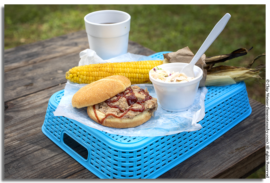 A BBQ pulled pork sandwich, coleslaw, and a fresh ear of grilled and buttered corn on the cob along with some sweet tea