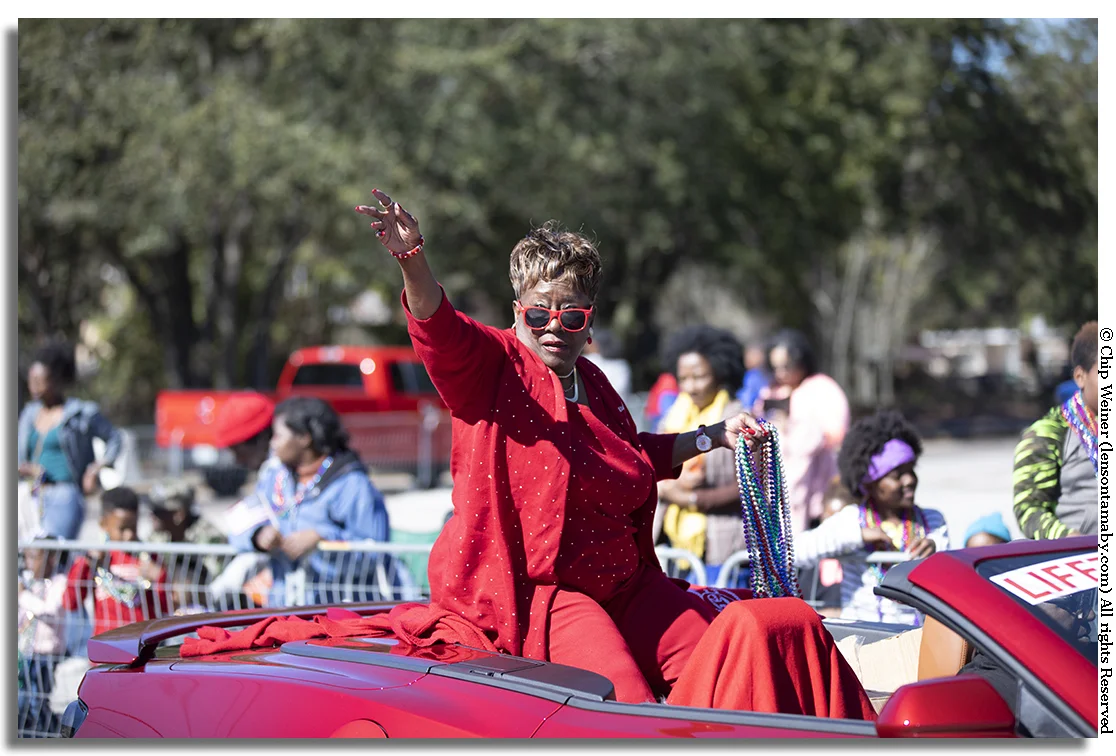 Parade Grand Marshall Dr Paulette Walker in her red sunglasses and red attire rides in a red convertible!