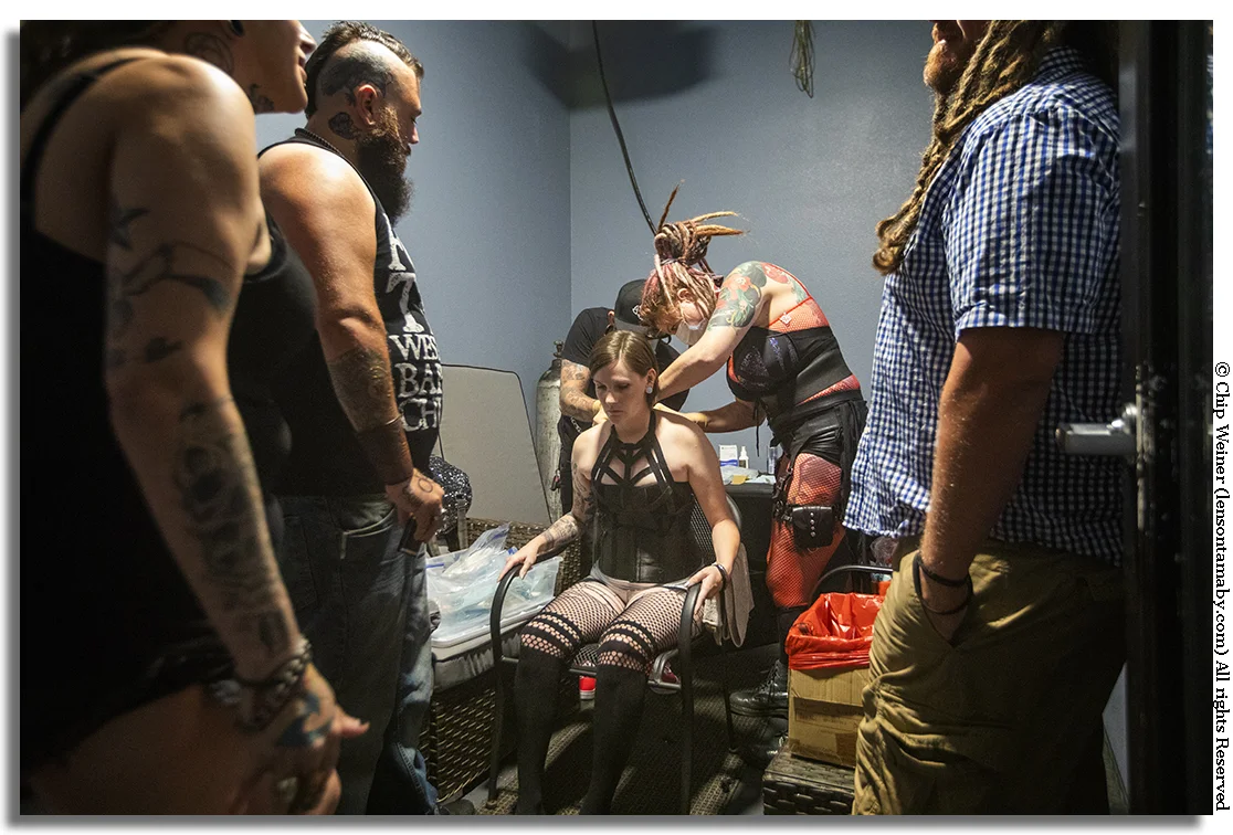 A suspension newcomer has hooks placed in her back before participating for the first time. The procedure is done with surgical skill.