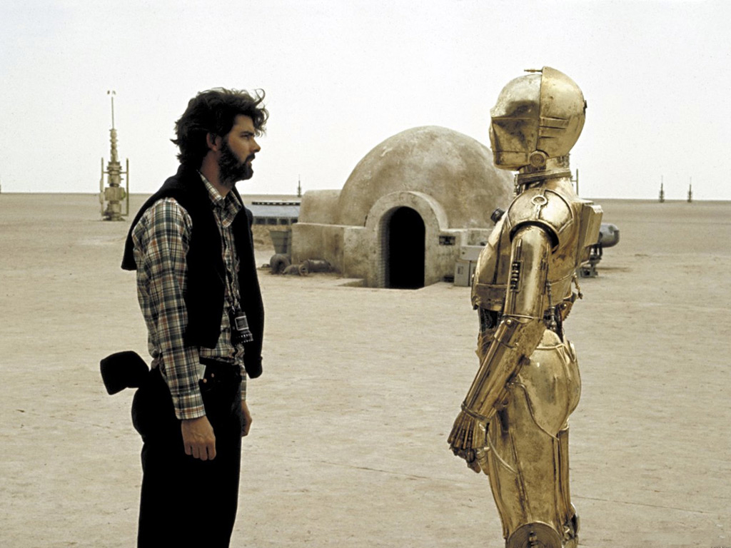 A young George Lucas confers with Anthony Daniels as C-3P0 on location in Tunisia, 1976.