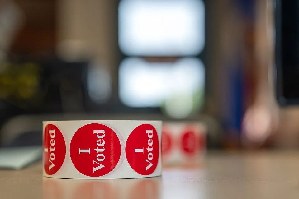 A roll of red "I voted" stickers on a table with a blurry background