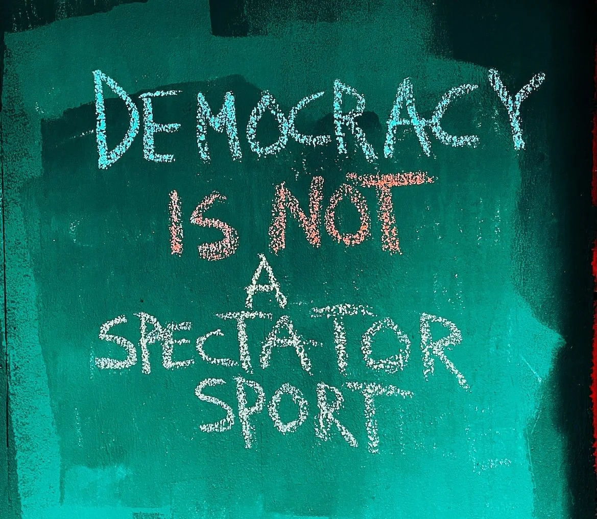 "Democracy is not a spectator sport" written in chalk on a green background