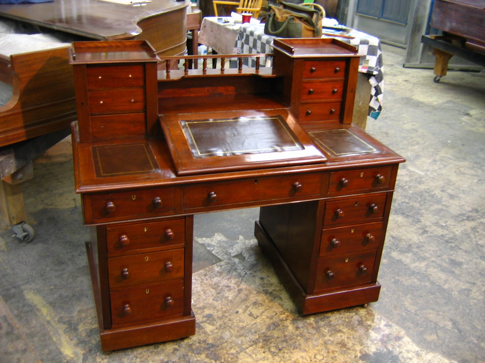 Antique wooden writing desk with multiple small drawers and a leather inlay on the top, situated in a vintage shop.