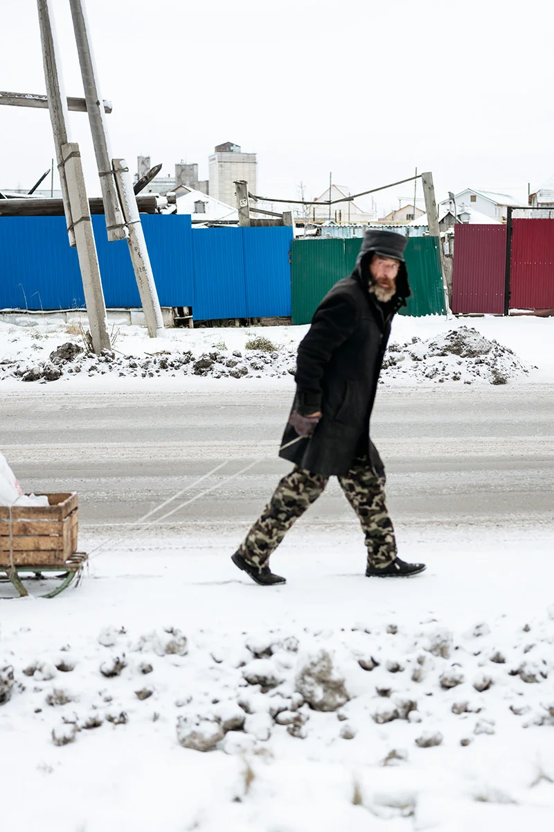 An old man carrying groceries and equipment in Tatarsk.