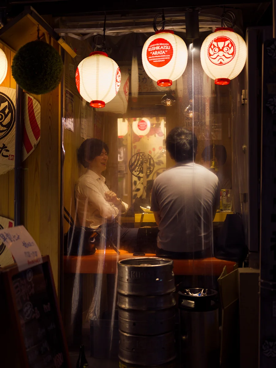 Seated tables in the outer area of the bar, there’s just a plastic cover replacing the window, allowing for the fresher air of the street to sneak in. Outside, empty jugs of beer are stored. Akasaka district (Minato).