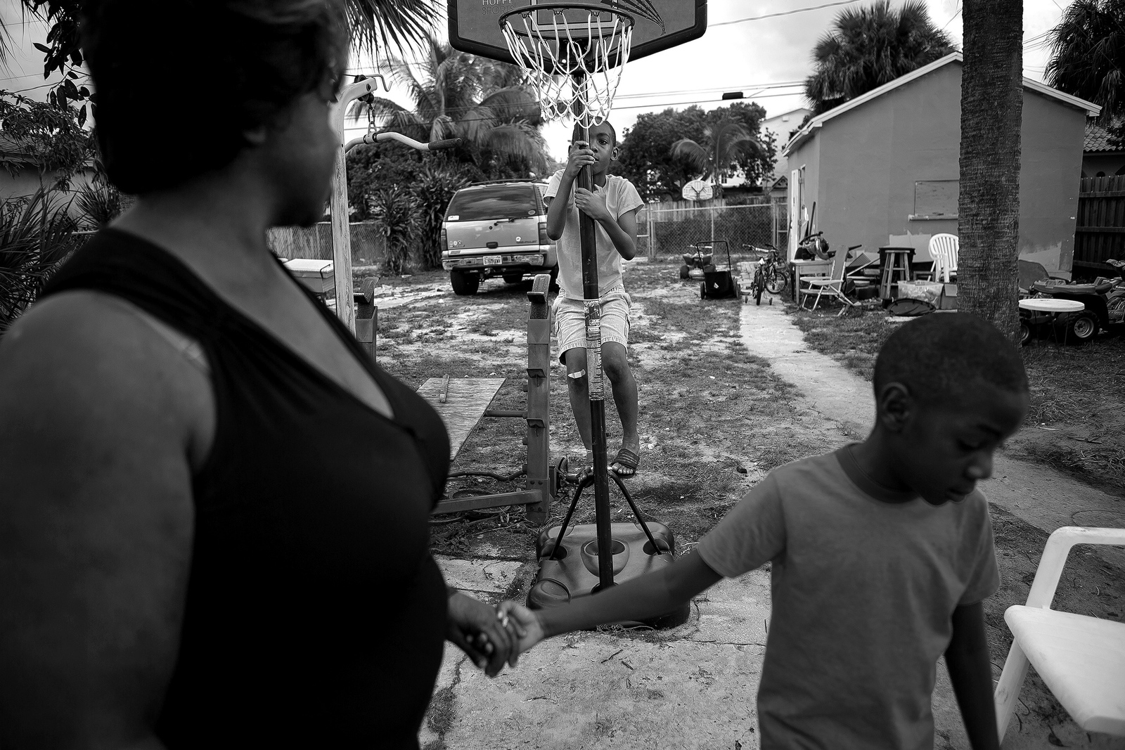  Omari Tripp, 8, climbs up the basketball hoop in his backyard as his brother Odarius, 6, pulls their mother Angeline back inside. Both Omari and Odarius have severe autism and require nearly constant supervision.&nbsp; 