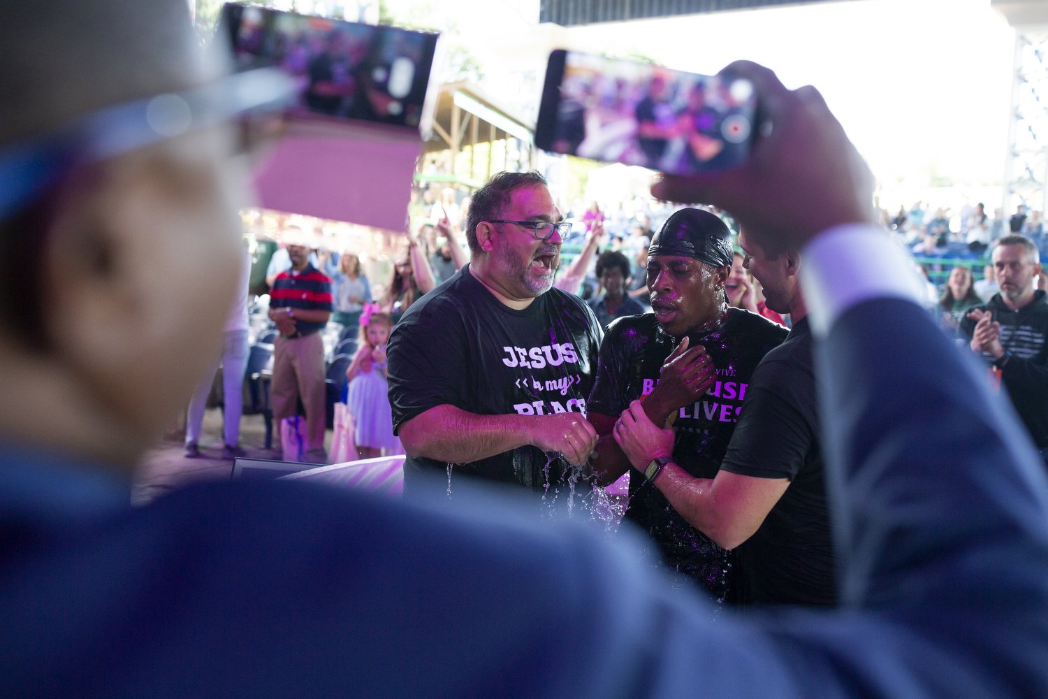  Emmanuel Kidibu is baptized during the Summit Church Easter Sunday service as his father Yabi Kidibu records the moment on two phones at Walnut Creek Amphitheater in Raleigh. Thousands of people attended to hear Pastor J.D. Greear deliver a sermon a