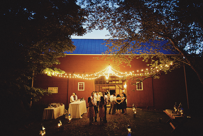 guests standing outside of red barn lit with string lights