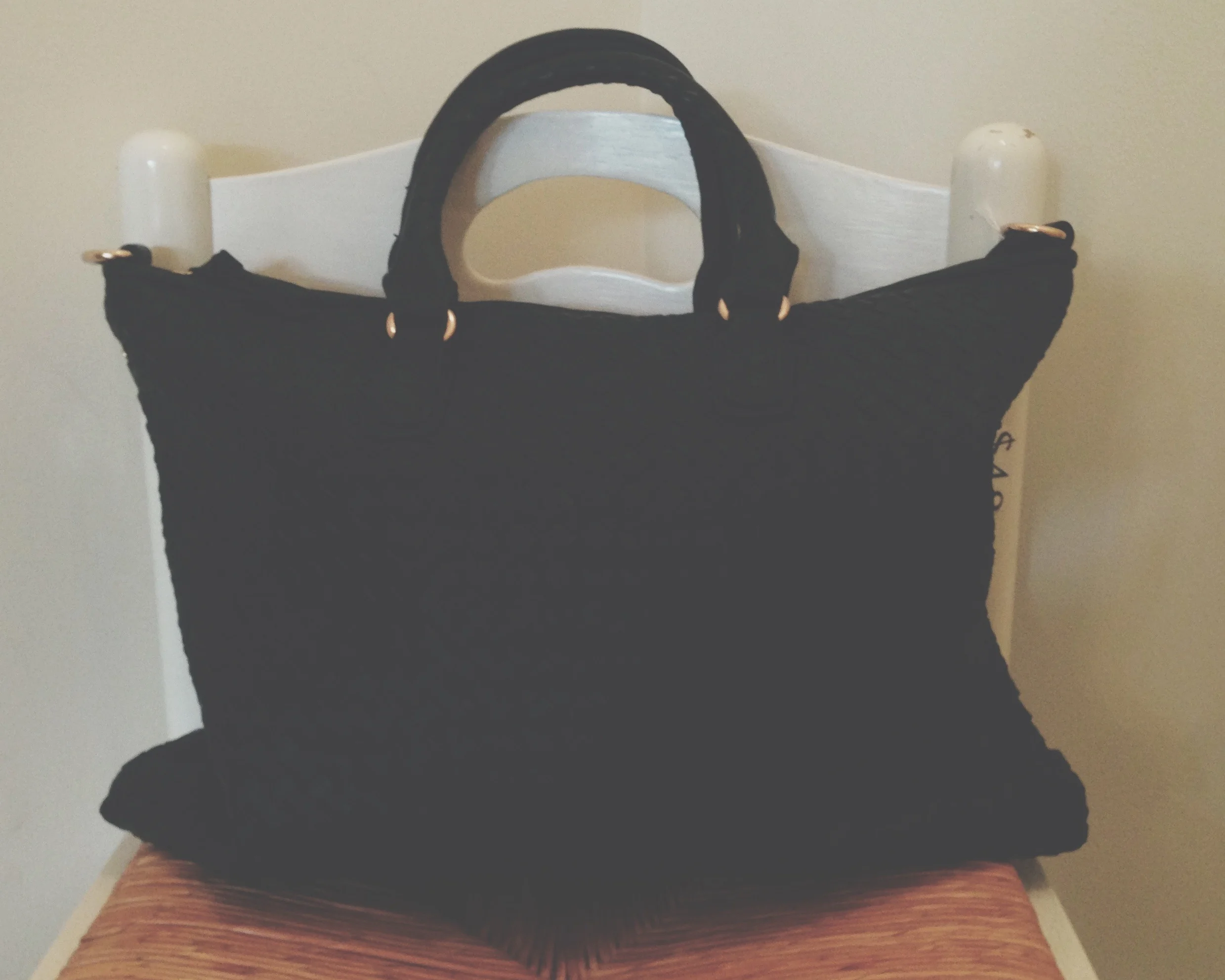 This black bag has intricate woven detailing. It comes with a long shoulder strap. It's the perfect size for a laptop bag.