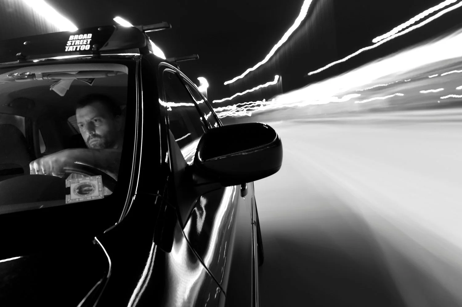 Black-and-white photo of a driver at night with light trails, by Joe Staska