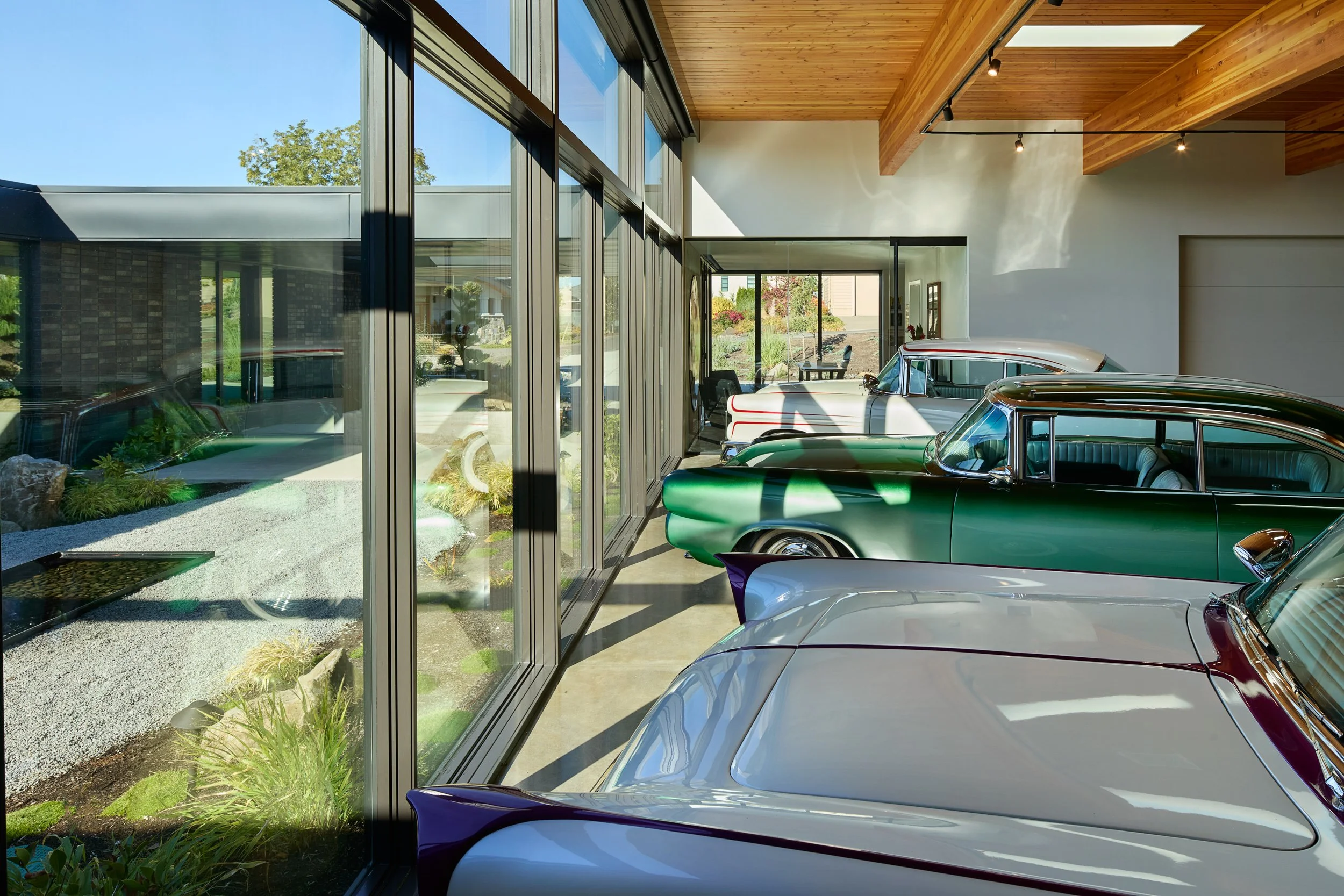 Car gallery with custom classic cars and view of courtyard — El Capitola residence by William Kaven Architecture