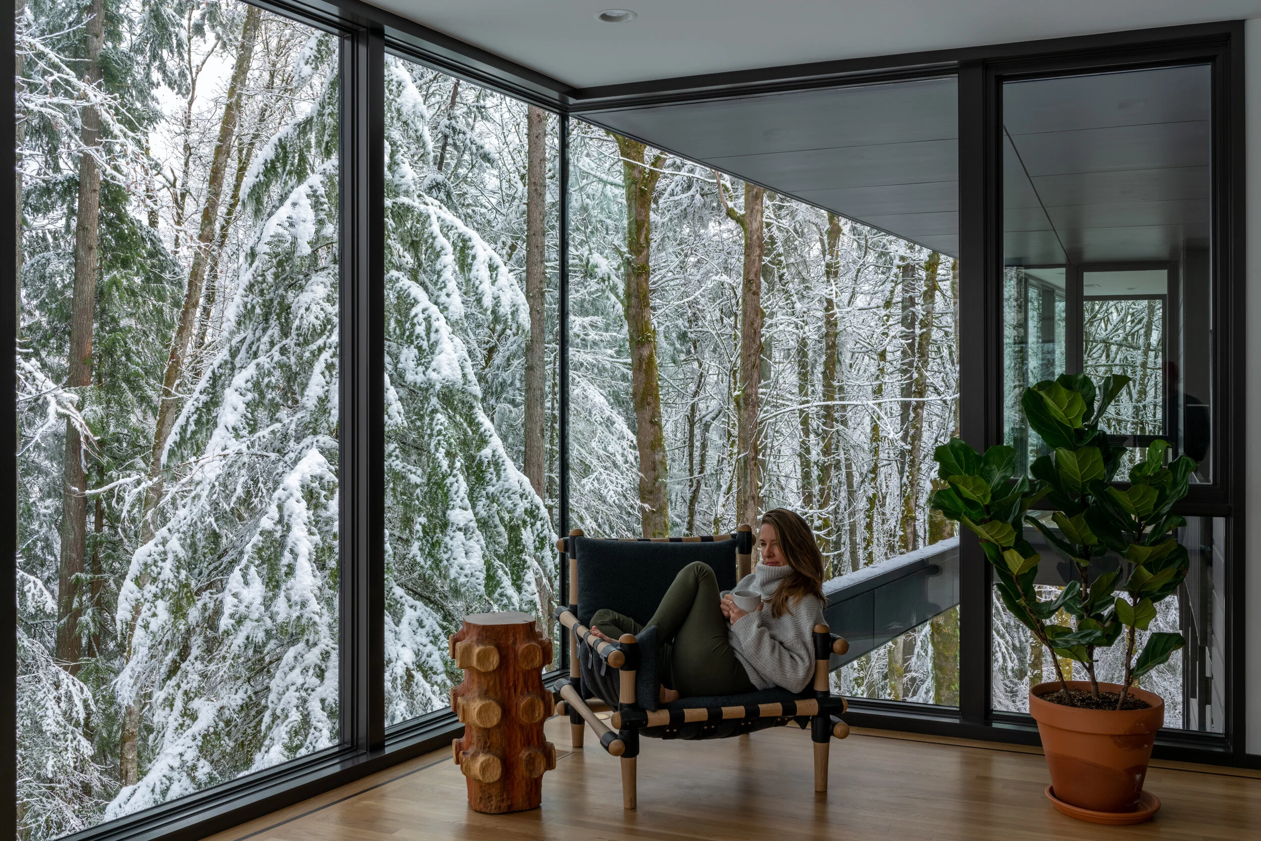 Woman in reading chair with snowy forest in background — William Kaven Architecture