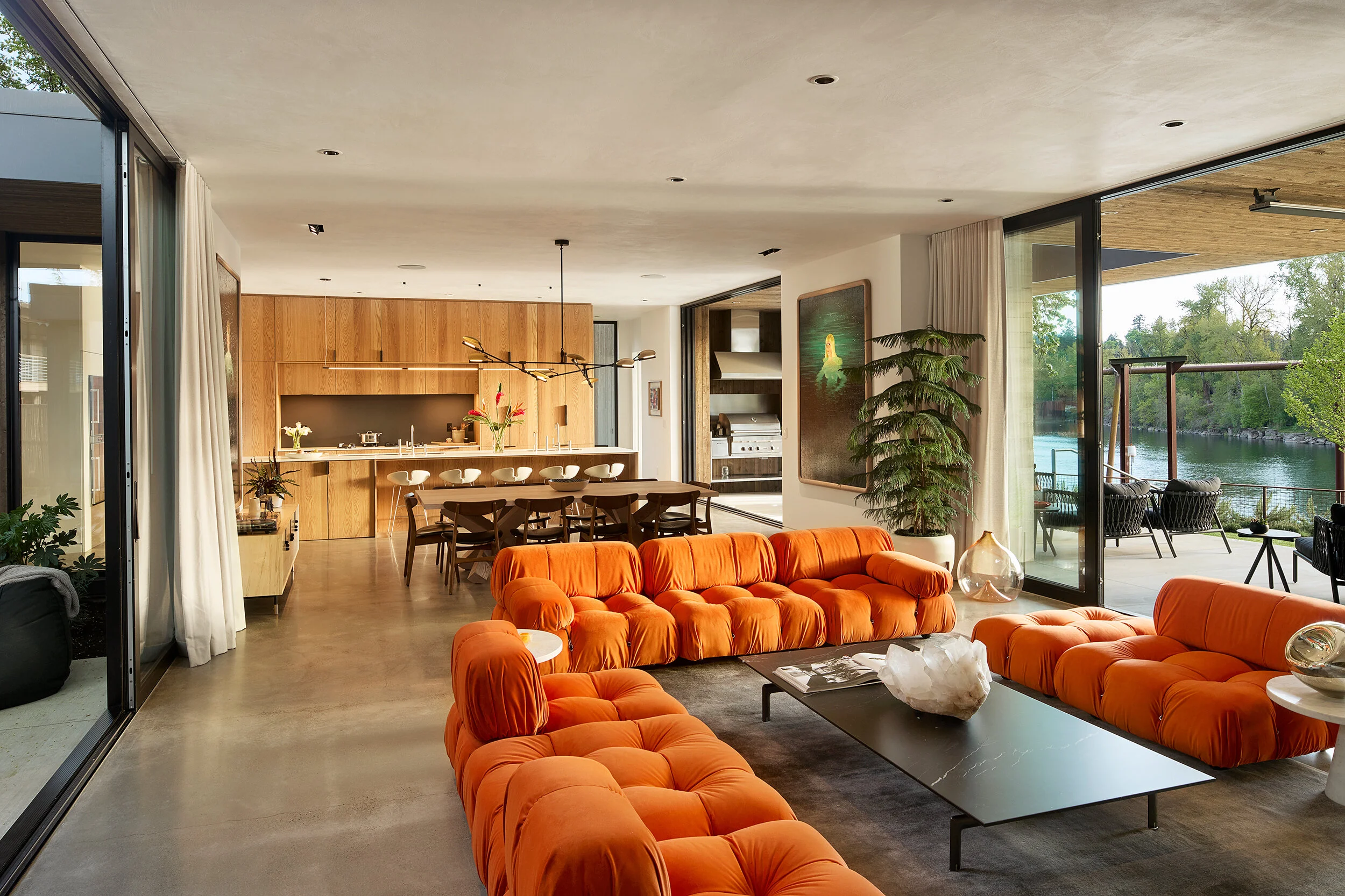 Modern living room with orange Mario Bellini Camaleonda sofa with view of kitchen and river — William Kaven Architecture