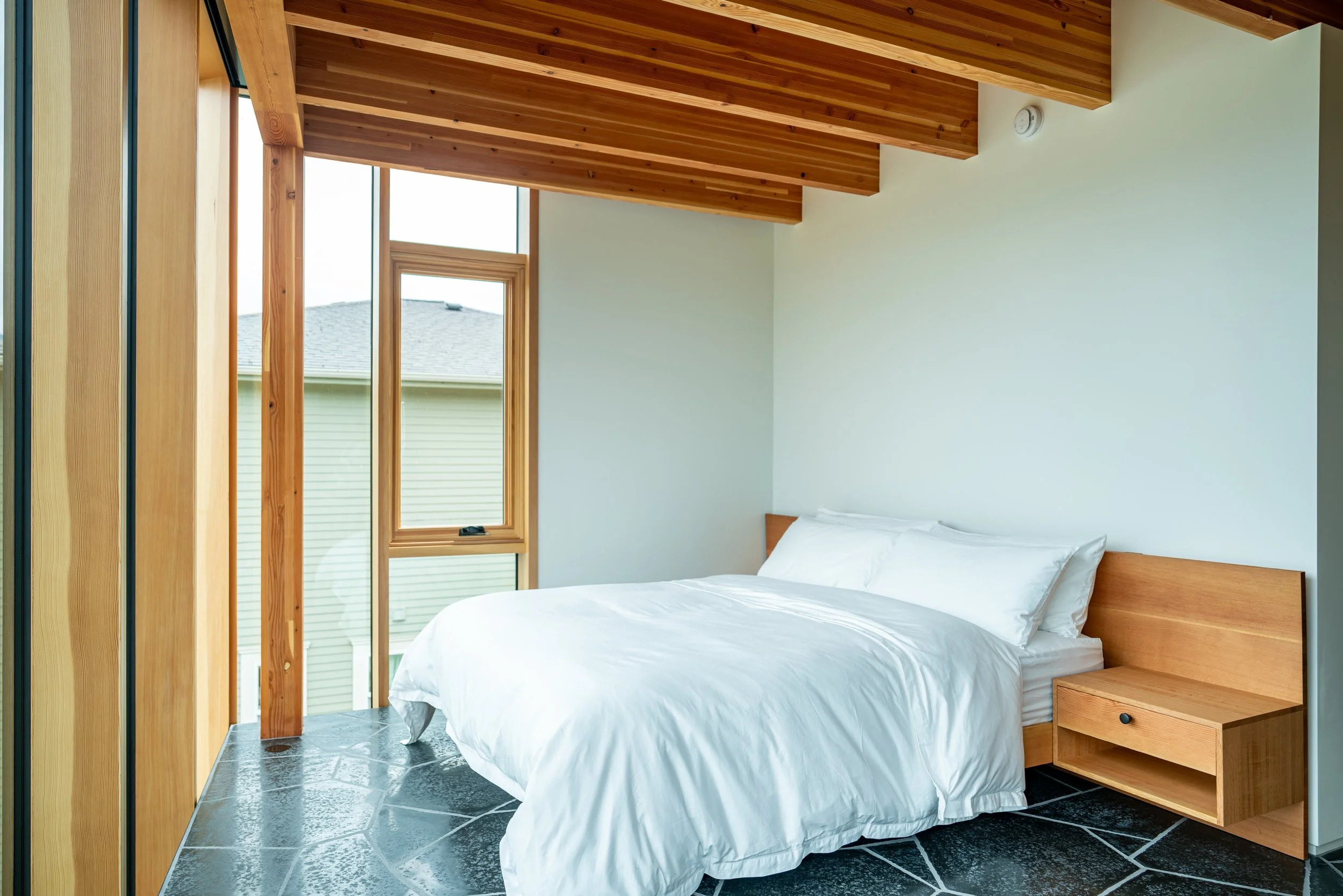 Bedroom at Hood River house with white bedding, white oak exposed ceilings, and basalt floors — William Kaven Architecture