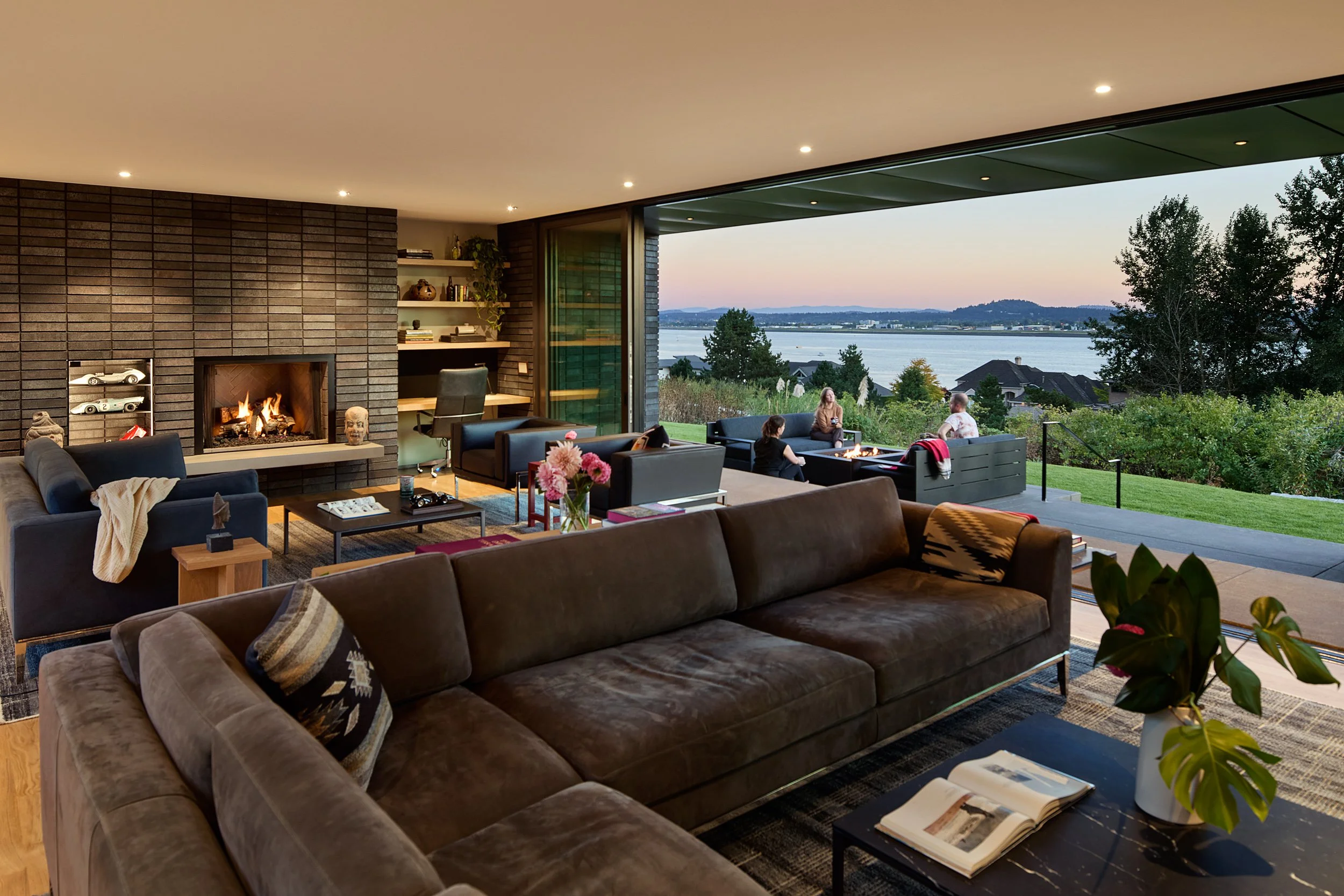 Living room with dark brick fireplace surround and river view — William Kaven Architecture.
