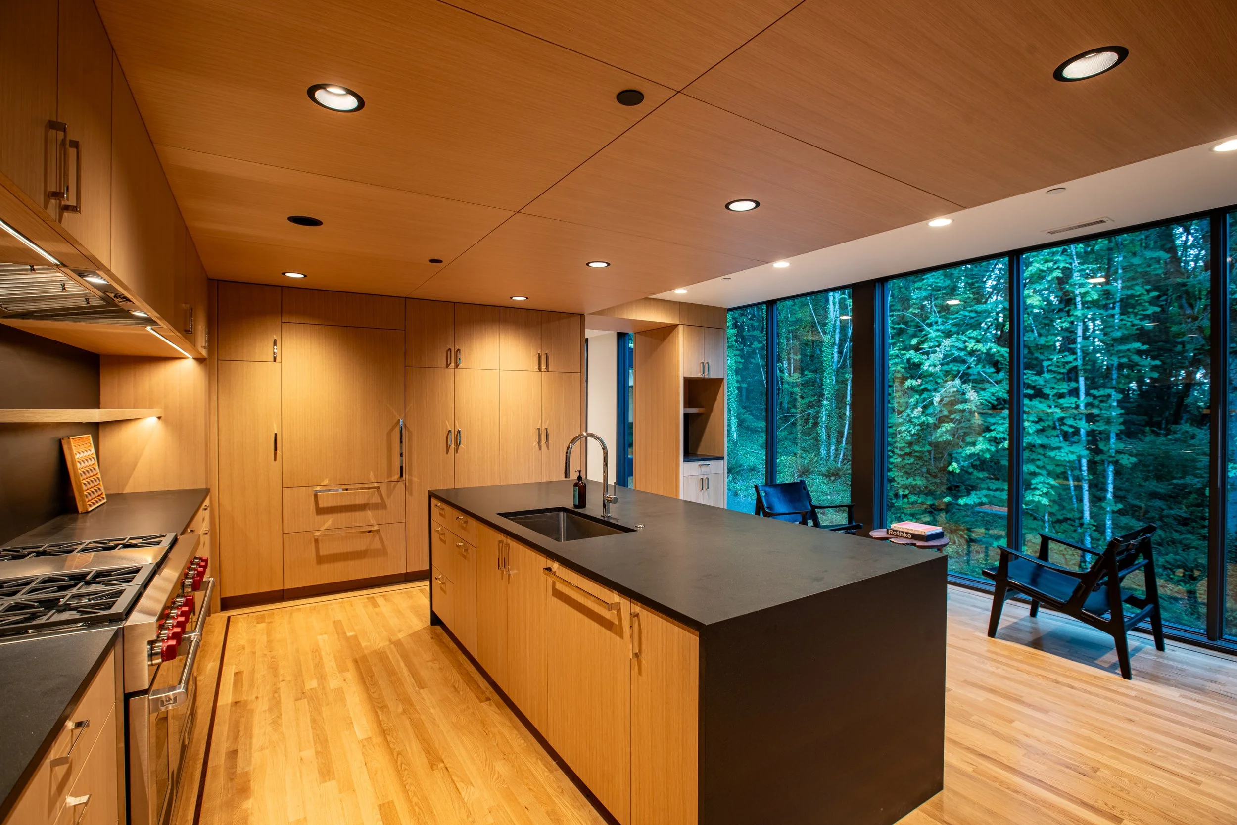 Modern kitchen with island and view of forest — William Kaven Architecture