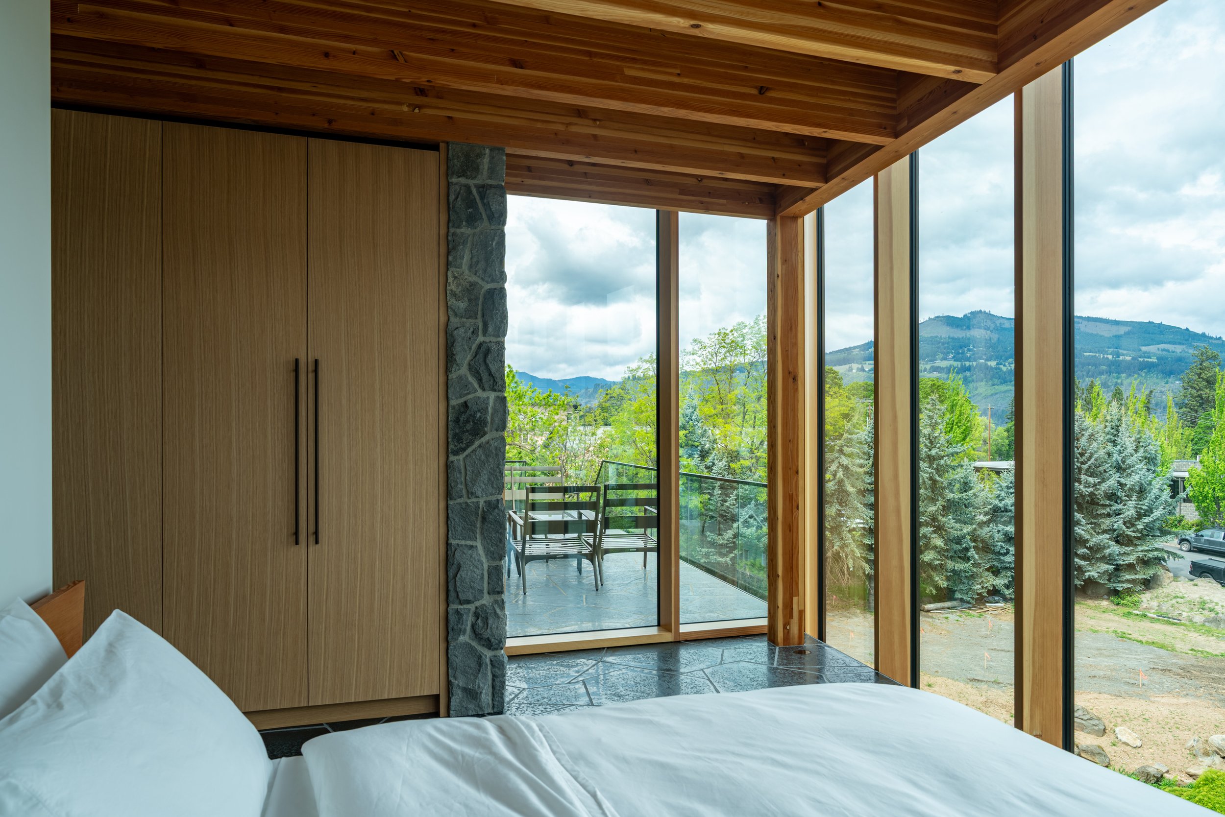Hood River house bedroom with stone wall and basalt floors — William Kaven Architecture