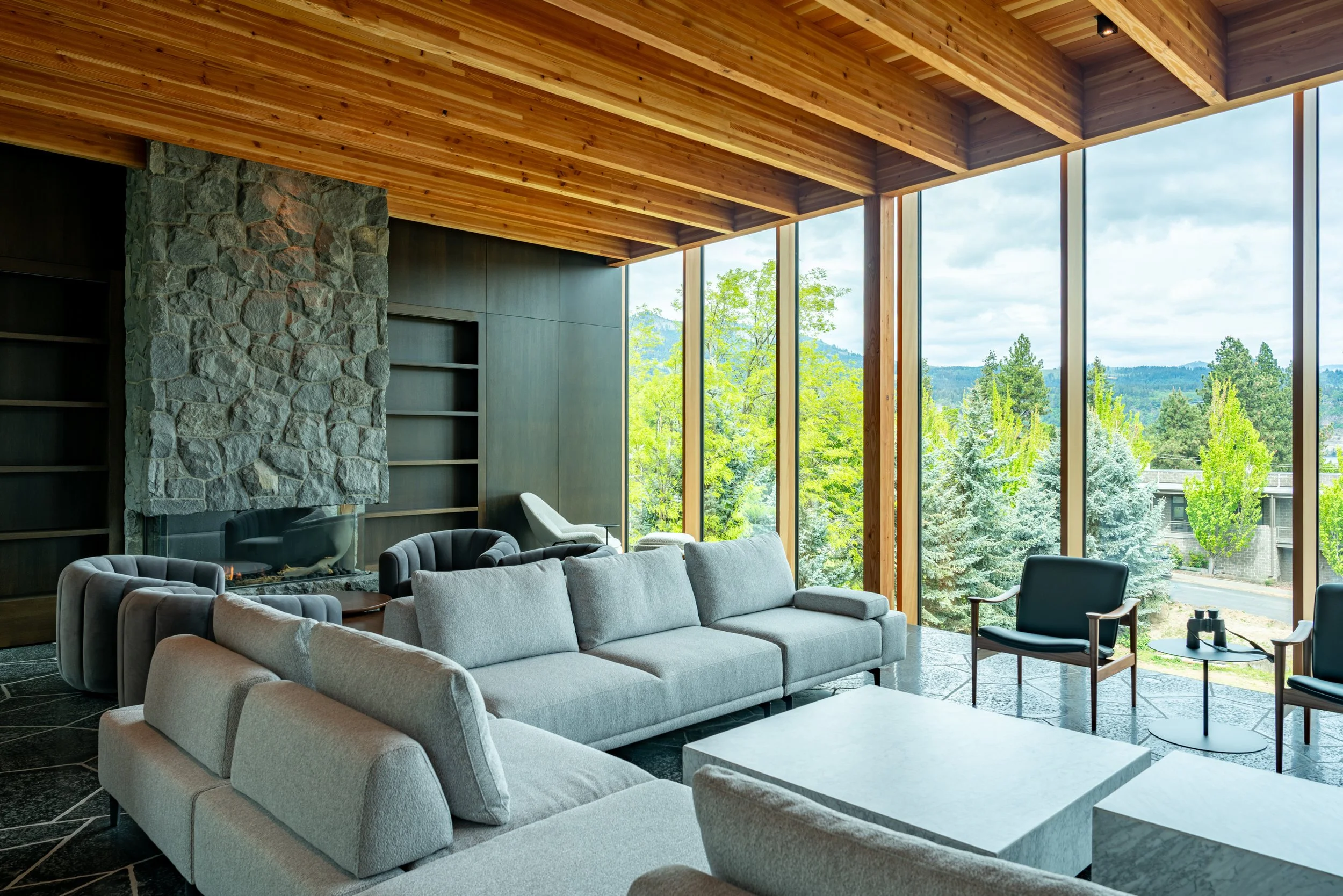 Living room at Hood River house with stone fireplace surround, dark wood walls, and basalt floors — William Kaven Architecture