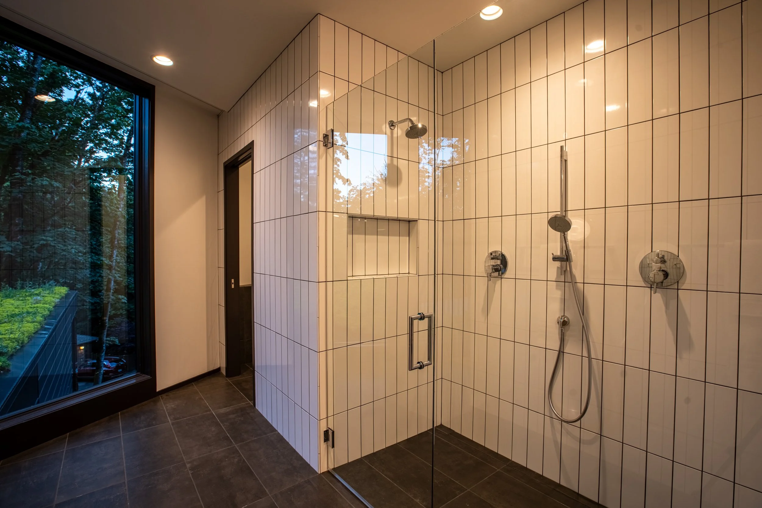 Shower with white tile and view of forest — William Kaven Architecture