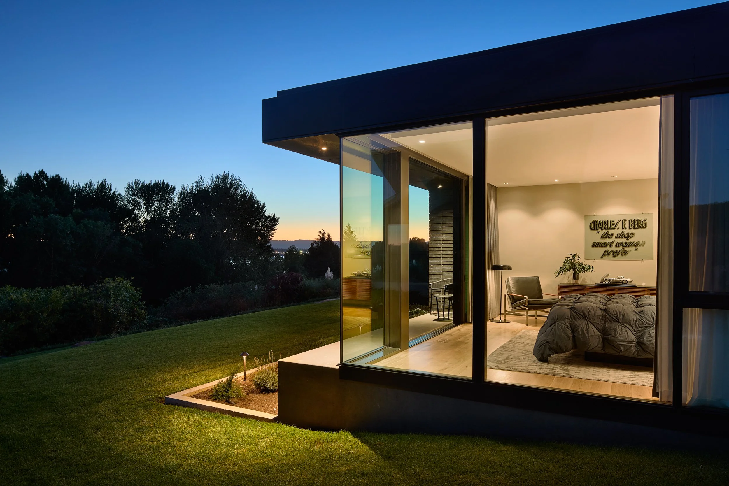 Well-lit corner bedroom at dusk with view of lawn and city — William Kaven Architecture.