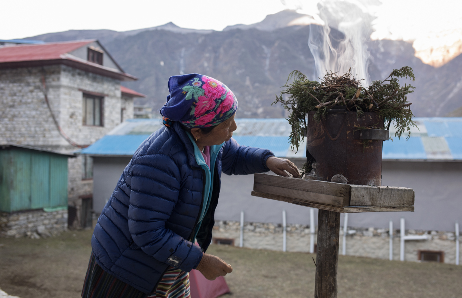 Pemba Yenji Sherpa delicately arranges burning embers below juniper branches during the last moments of sunrise in Namche Bazzar, Nepal. The branches are burned as incense for good luck.