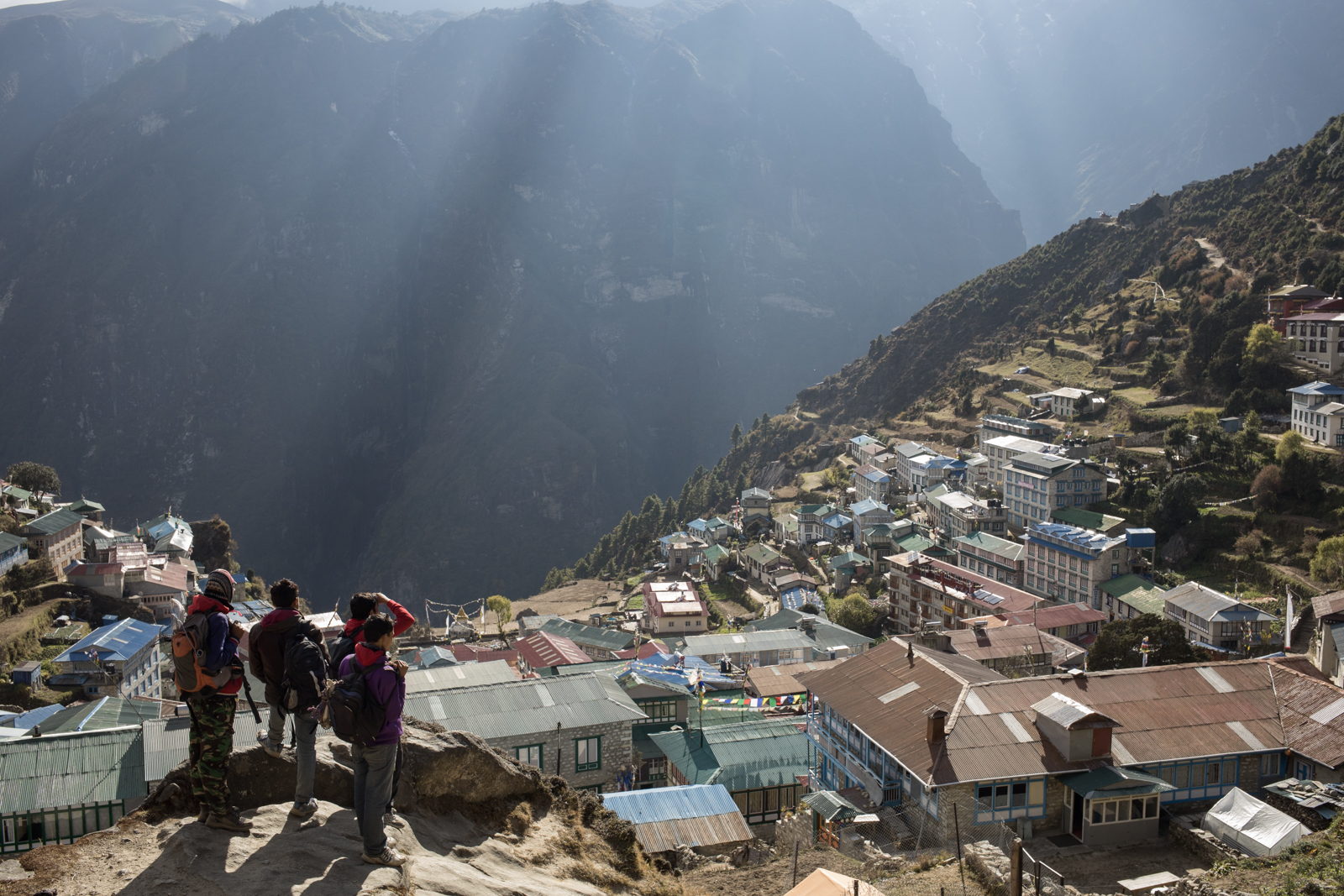 A group of young men look out over the village of Namche light breaks through the clouds.