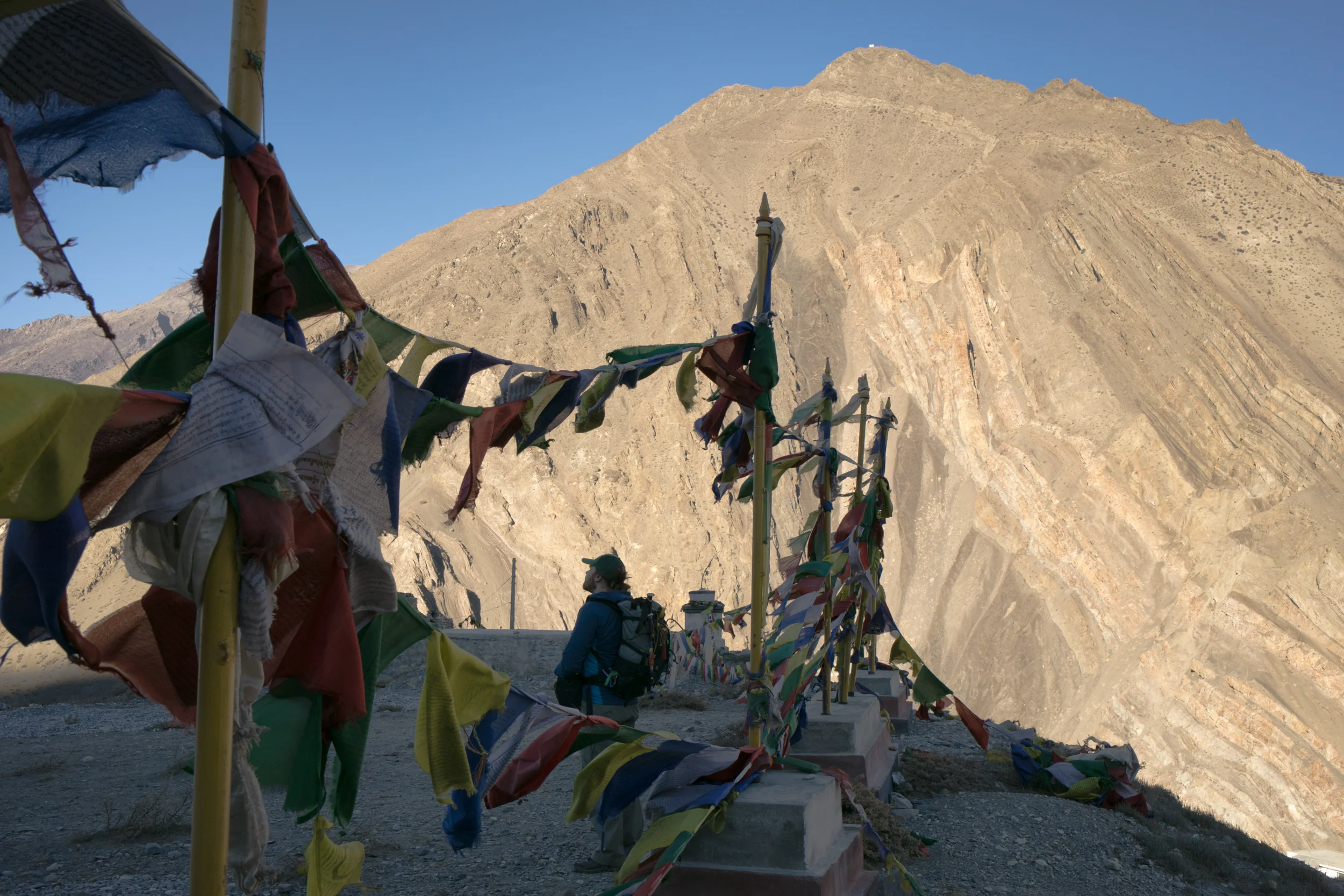 Aaron stands on a ridge with Prayer flags as the morning sun spreads across the distant peak. 