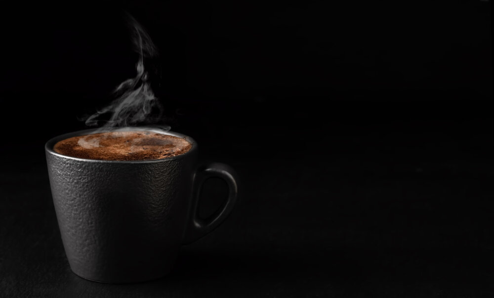 A wisp of steam against a dark background, and warm tones, leave no doubt this cup of coffee would be a satisfyingly hot sip.