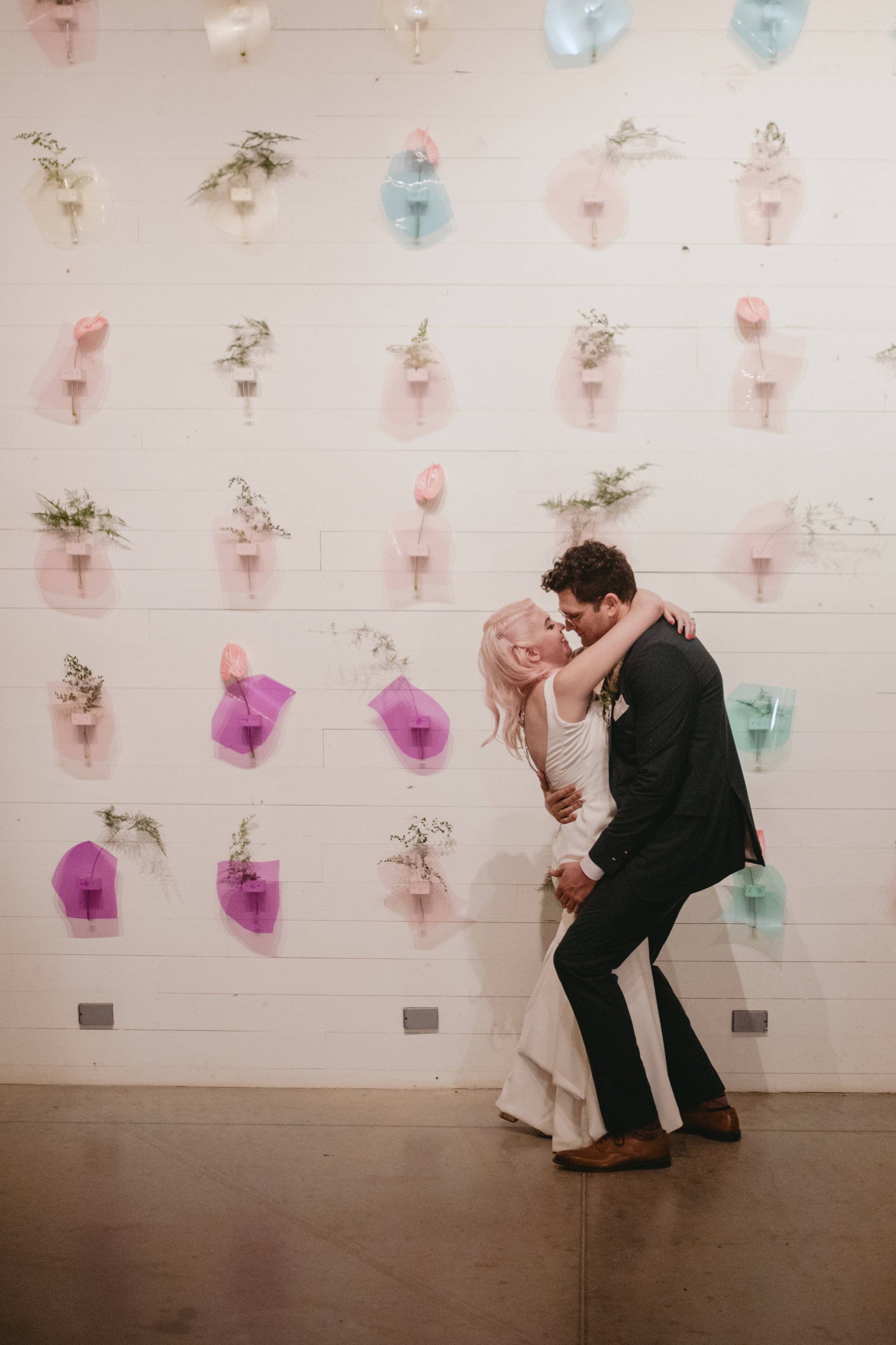 Bride with pink hair and groom in a purple suit prospect house wedding in austin tx with pastel decor and wild florals flower wall kiss