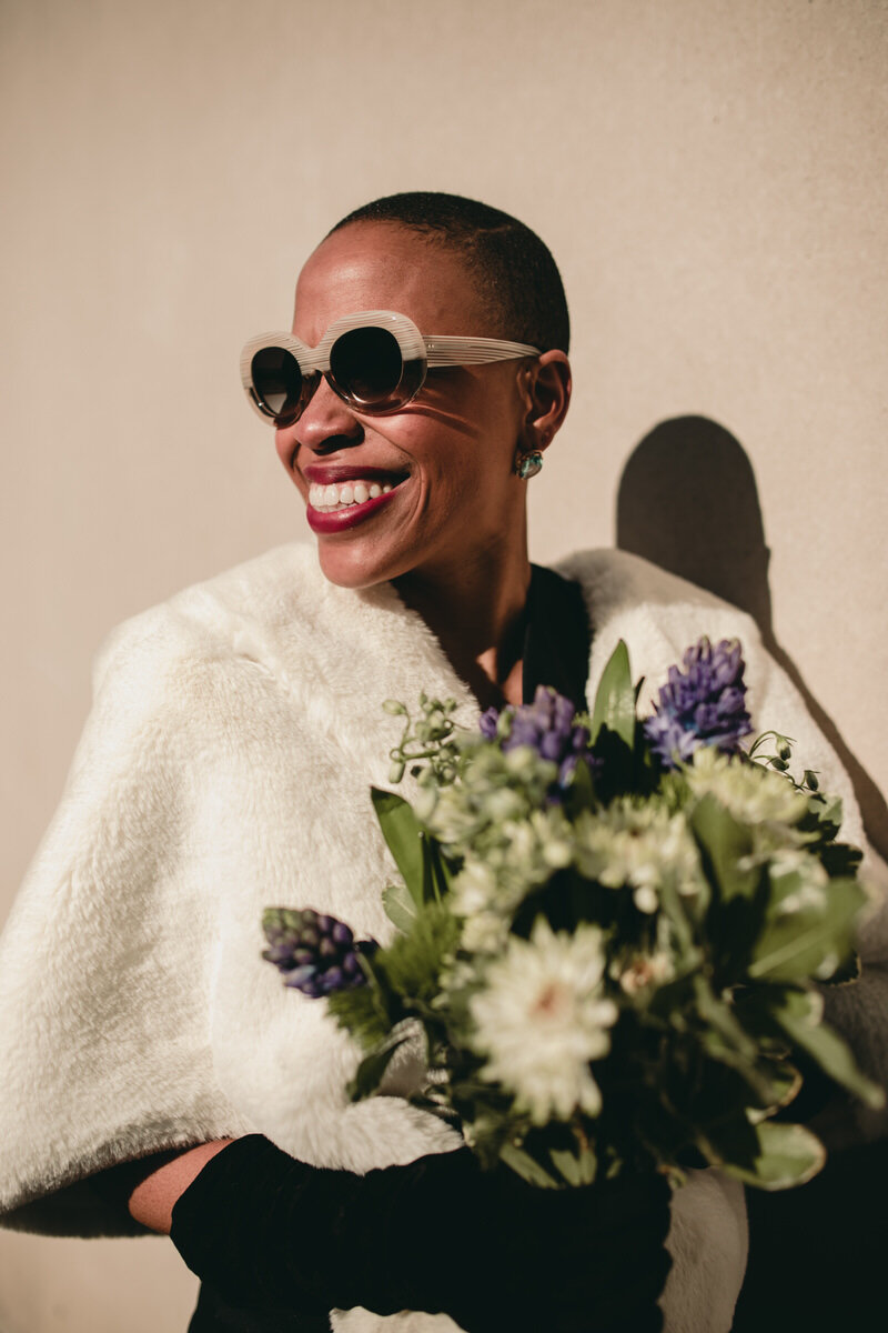  Black Woman on her Wedding Day Smiling with flower bouquet and sunglasses at the Virginia MFA, in Richmond, by Carly Romeo 